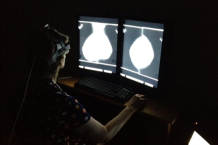 A radiologist outfitted with a head-mounted eye-tracking device examines a mammogram